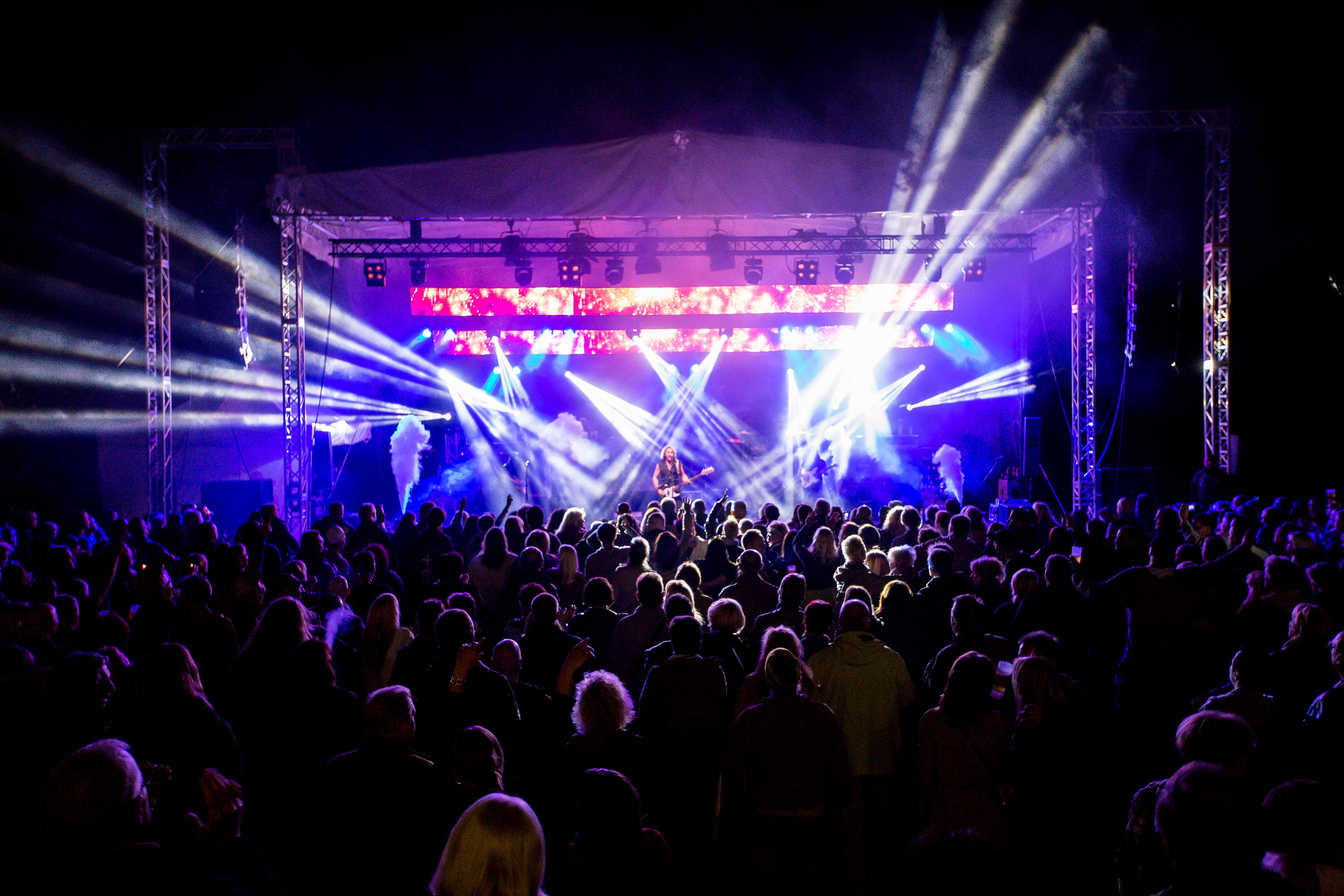 Konzertveranstaltung auf der Freilichtbühne Wattenscheid. Von der Bühne strahlt Licht aus vielen Scheinwerfern ins Publikum. Die Bühne ist blau und lila beleuchtet.