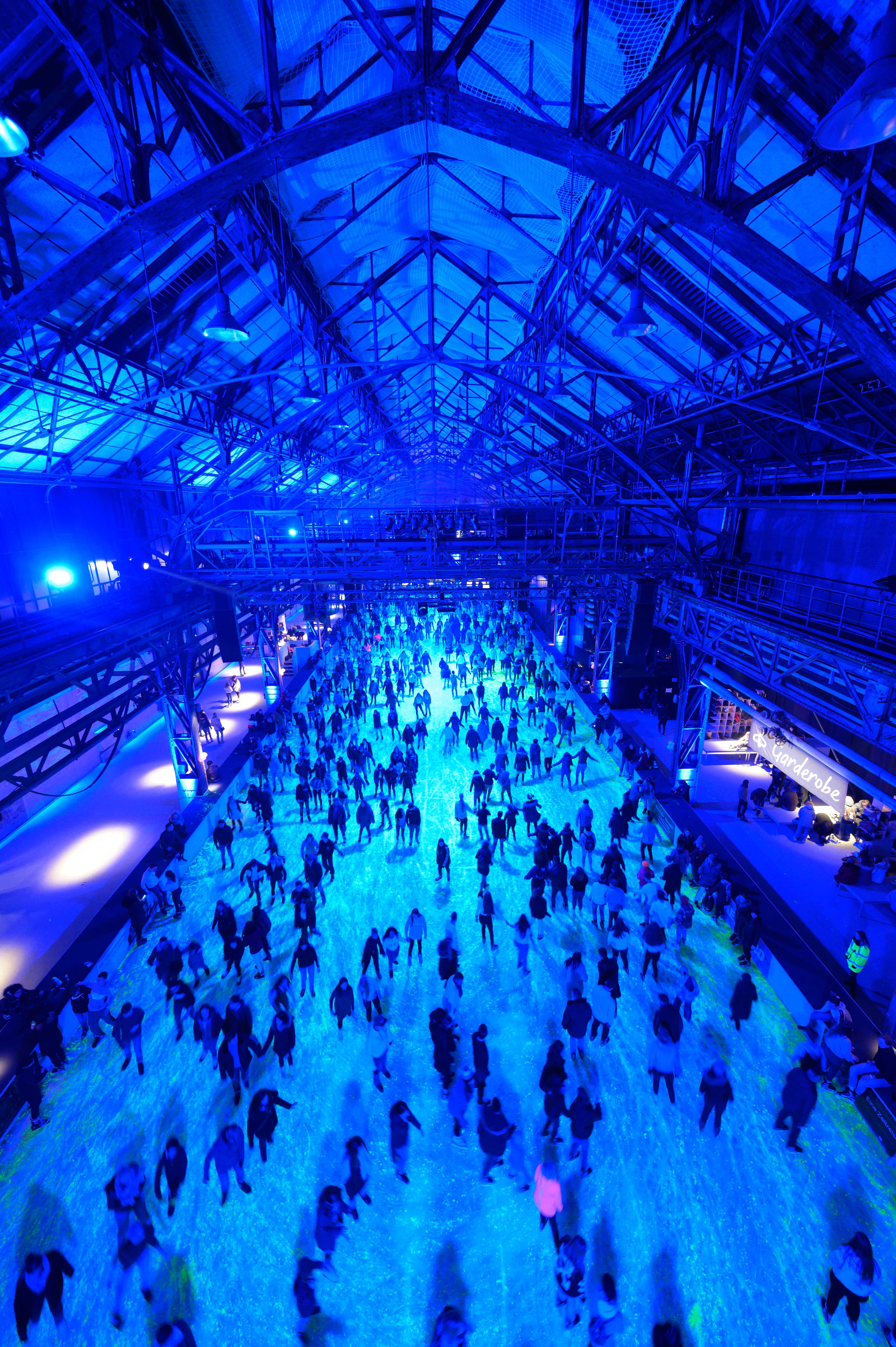 Blick auf die gut besuchte Eisbahn des EisSalon Ruhr in der blau beleuchteten Halle 1 der Jahrhunderthalle Bochum.der Halle 