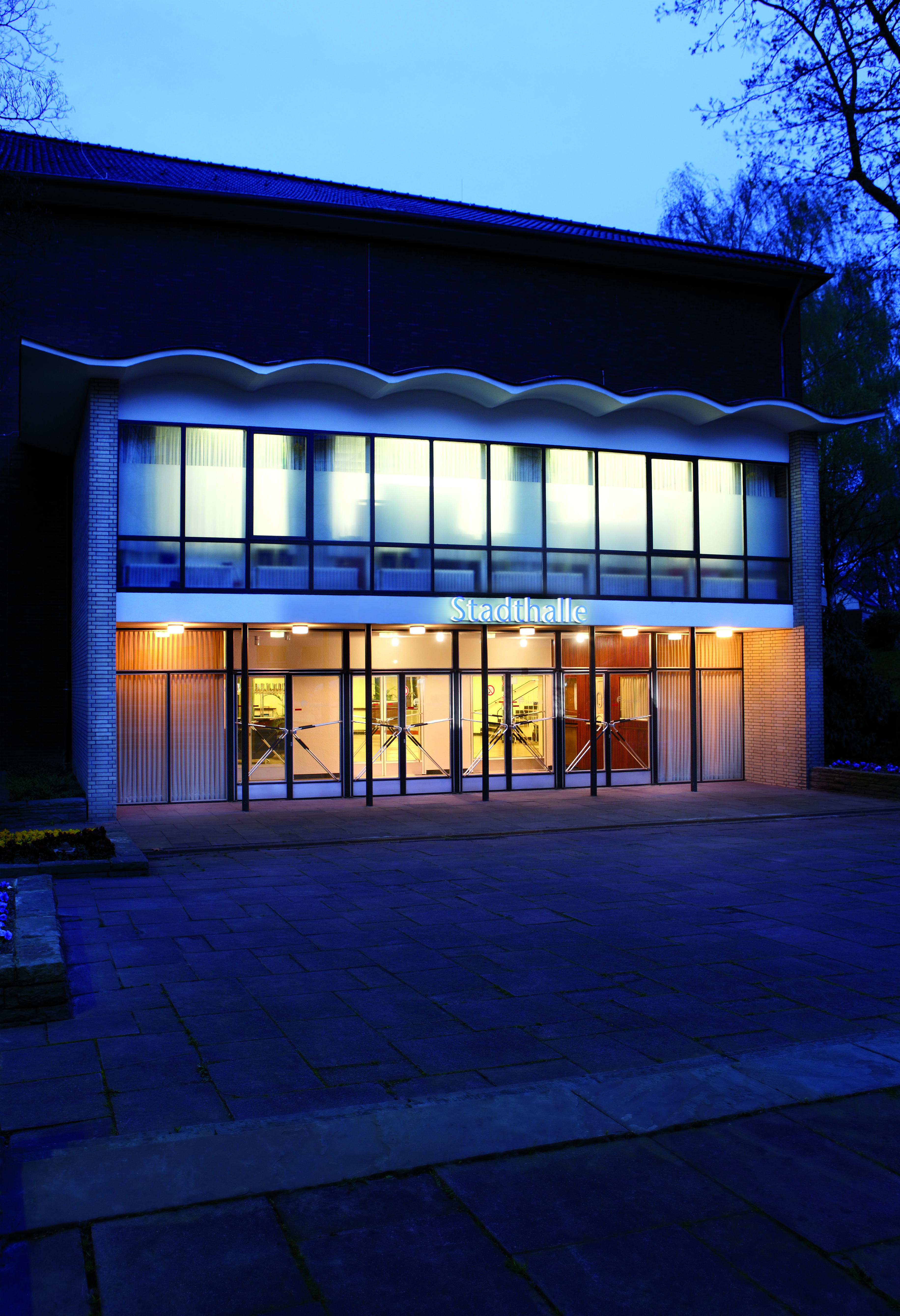 Außenansicht des beleuchteten Haupteingangs der Stadthalle Wattenscheid zur Zeit der blauen Stunde.